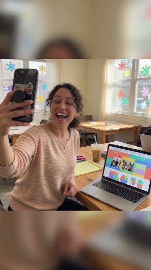 A nonprofit director filming herself on a phone at a classroom table, with her organization's website open on a laptop beside her.